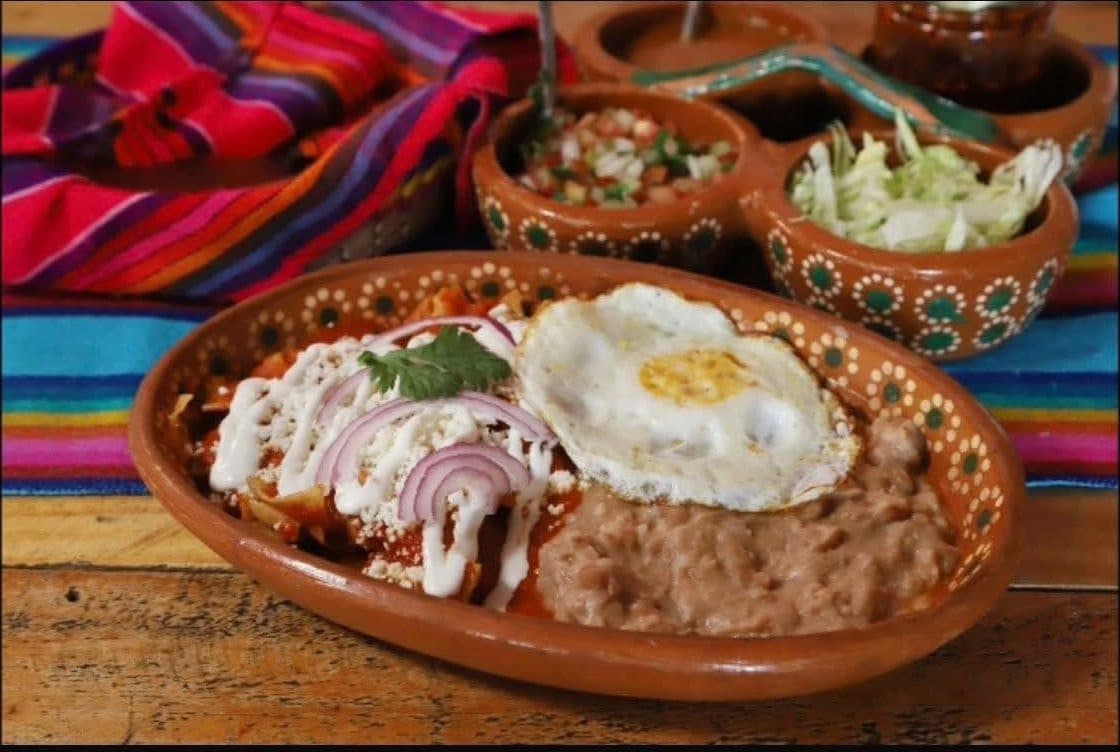 Chilaquiles rojos con huevo y frijoles servidos en plato de barro