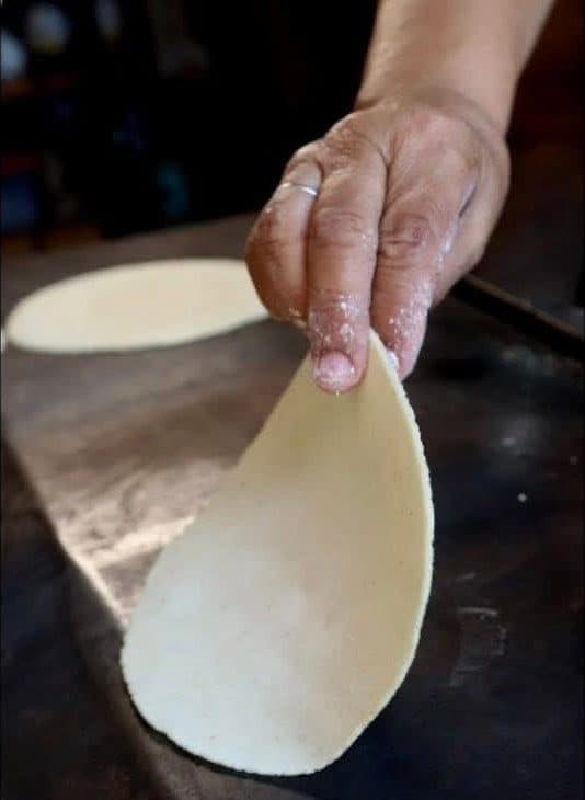 Manos haciendo tortillas a mano sobre el comal